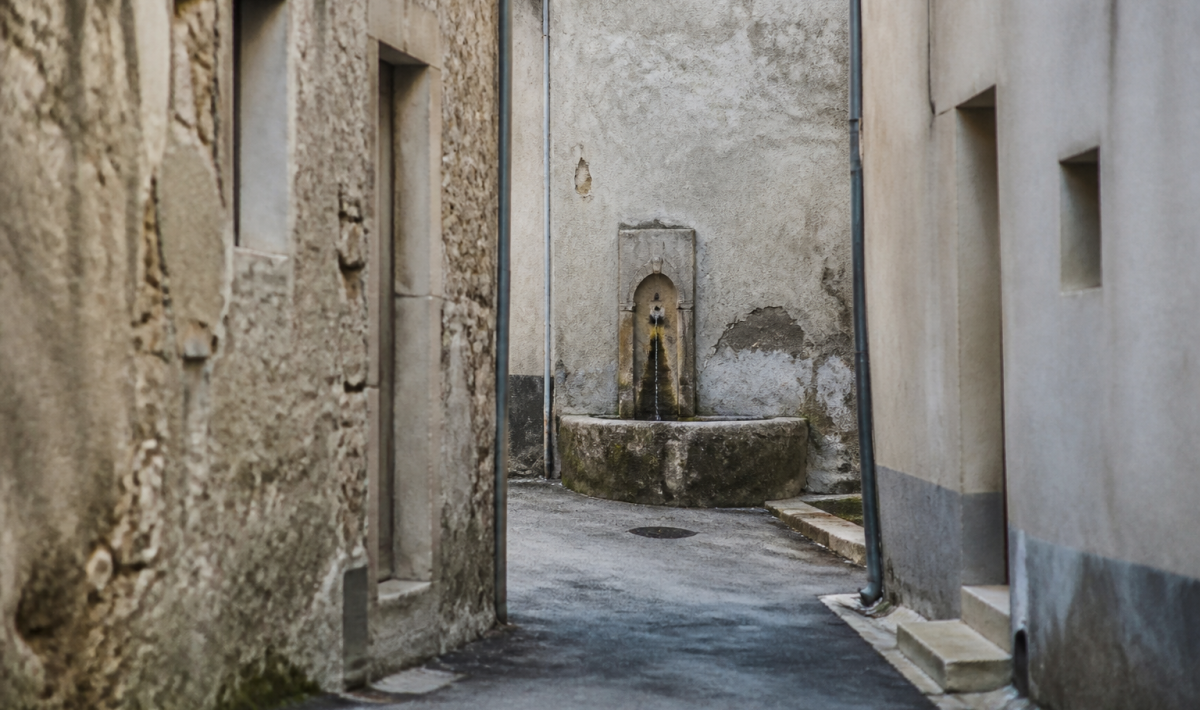 rue etroite fontaine bâtiments délabres murs gris fissurés